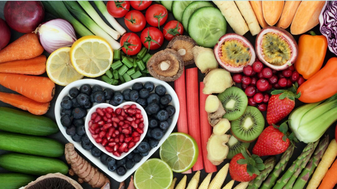 Fresh fruits and vegetables arranged with a heart-shaped bowl of berries.