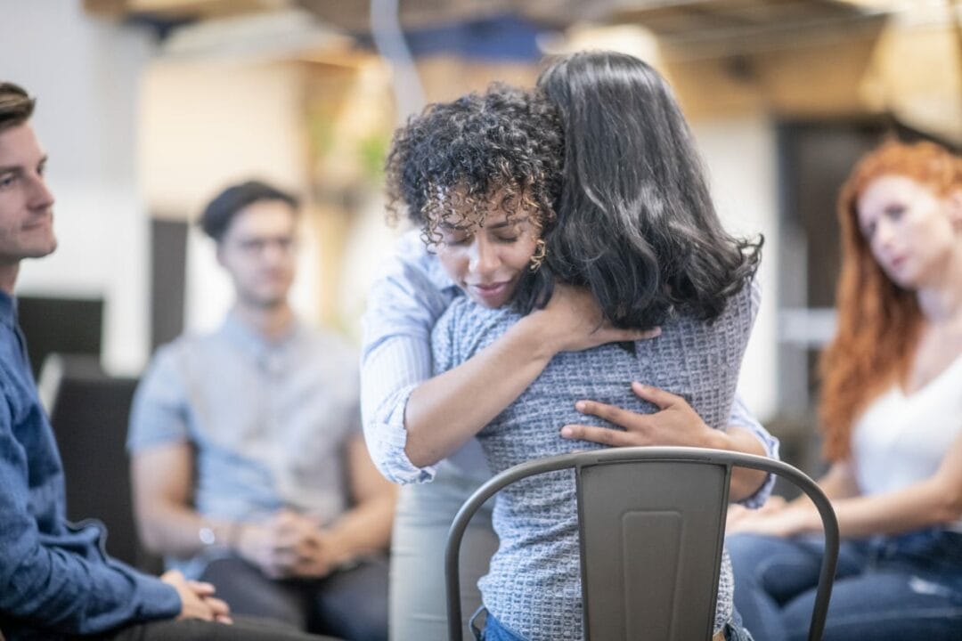 A woman is hugging another woman in a meeting.