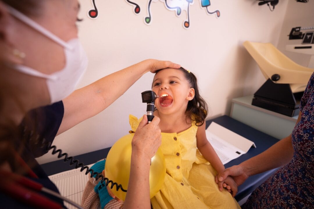 A little girl is getting her throat inspected by a doctor.