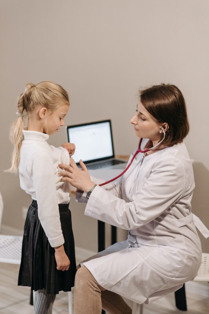 A woman in a white coat is examining a little girl's heartbeat.