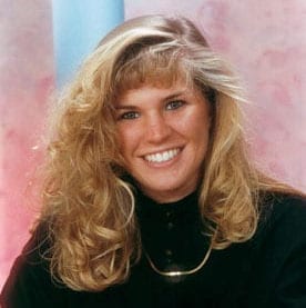 A woman named Stacy McKay with long blonde hair sitting in front of a pink background.